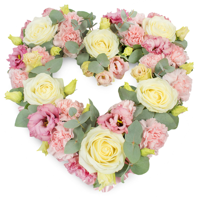 A full, heart-shaped funeral wreath is presented against a clean, white background, its pastel blossoms and cool greenery combining to create a soothing, elegant tribute that reflects the composed charm of Northwood and nearby Moor Park. The heart itself is perfectly formed and symmetrical, each curve traced by flowers placed so closely that no space is left uncovered. Cream and pale yellow roses anchor the design, their velvety petals spiralling outward from firm centres, capturing the enduring nature of love and respect. Around these focal blooms, clusters of pastel pink carnations tumble softly, their ruffled, layered petals adding a gentle, billowing texture that suggests comfort and emotional warmth. Deeper splashes of colour come from magenta and mauve lisianthus, whose slightly open, trumpet-shaped flowers bring subtle drama, like the soft intensification of colour at sunset over Northwood's leafy skyline. Silvery-green eucalyptus leaves weave in and out of the blossoms, their rounded form and frosted tone offering a cool, calming counterpoint to the roses and carnations. Threaded discreetly through the composition are small yellow-green buds, which suggest renewal, continuity, and the quiet persistence of hope. The flowers are arranged in a dense, unified layer, so the heart appears lush and luxurious yet never overwhelming, just serenely complete. This wreath feels like a thoughtful choice for families in Northwood seeking to express condolences with grace-ideal for placing at the front of a chapel, adorning a crematorium service, or resting at a graveside. It conveys sympathy, remembrance, and a gentle, abiding love for the person being honoured, without harsh colour or sharp line to disturb the sense of peace.